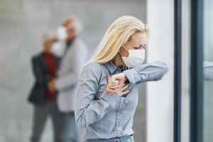 A Business Woman With Protective Mask Coughs At The Elbow During COVID-19 Pandemic