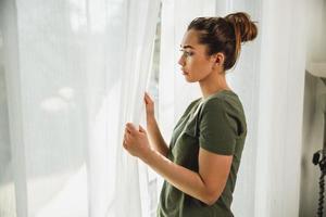 Woman Feeling Worried While Standing Near The Window At Home photo