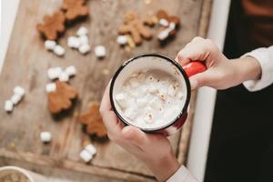 a cup of cocoa with marshmallows close-up, against the backdrop of Christmas cookies. Christmas sweets with cocoa and marshmallows for children on a wooden background. Winter vacation at home. photo