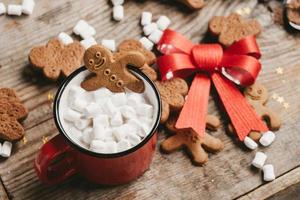 ginger man in a cup of cocoa with a big red bow on a wooden background, top view. Various Christmas sweets with a cup of cocoa on the table. Christmas flatlay photo