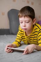 a teenage boy lies on the couch with a phone in his hands. The child plays at home in the phone. Recreation with the phone. Holidays with gadgets. photo