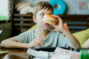 boy eating a big burger with a cutlet. Hamburger in the hands of a child. Delicious and satisfying chicken cutlet burger. Takeout food photo