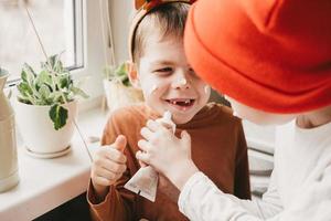 los niños con cuernos navideños se pintan la cara con glaseado blanco. divertirse en la cocina. vacaciones de invierno con niños. la payasada antes de navidad foto