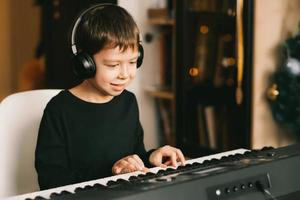 a boy in wireless headphones plays the piano, against the background of a Christmas garland photo