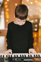 un niño con una camiseta negra toca el piano, en el contexto de una guirnalda navideña foto
