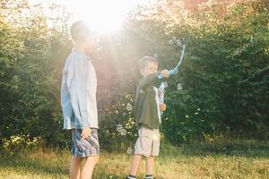 Boys play with soap bubbles in a summer park, Among the greenery. Happy children catch soap bubbles. photo