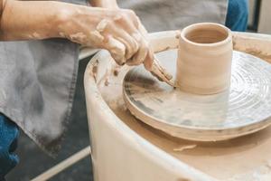 A girl with long hair sculpts a clay pot on a potter's wheel from a special wooden tool. Creative workshop. The women sculpts from clay. Working atmosphere in the workshop photo