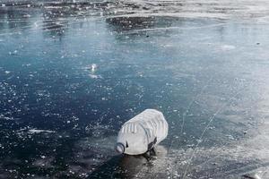 Winter ice structure with cracks. Garbage in nature. Plastic in a frozen lake photo