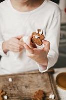 ginger man in white glaze in the hands of a child, close-up, on a white background. The gingerbread man is bathed in cocoa. Christmas mood. Christmas sweets and drinks, copy space photo