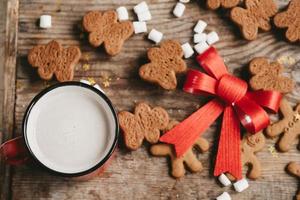 gingerbread man, cocoa and cookies with a big red bow on a wooden background, top view. Various christmas sweets with a cup of cocoa on the table photo