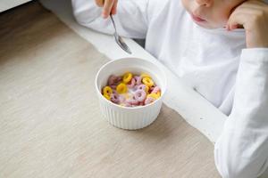 child eats colored cereals at the table, in a white kitchen. Boy's breakfast. Breakfast cereals before school. A quick snack of a schoolboy in the morning. photo