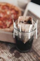 brewing coffee in a drip bag in a transparent glass, on a wooden background. Hot ground drip coffee, top view. Ground Ethiopian coffee in a reusable drip bag. photo