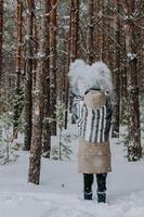 Tossed snow in the form of a heart in the air. A girl in a striped scarf stands in a winter forest and throws snow in the air. A girl stands with her back in the woods in a wide striped scarf. photo
