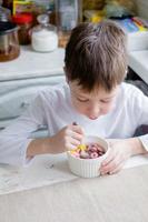 child eats colored cereals at the table, in a white kitchen. Boy's breakfast. Breakfast cereals before school. A quick snack of a schoolboy in the morning. photo