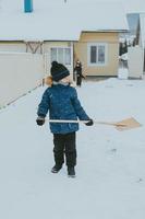 boy cleans snow with a shovel on the street. A boy clears the road from snow in winter. Hardworking child. A boy living in the village cleans the snow. photo