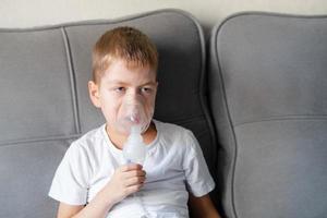 un niño pequeño se sienta con una máscara de inhalación durante la tos y la bronquitis foto