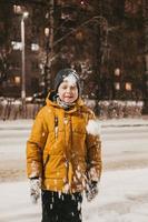 a boy in a yellow jacket plays with snow during a snowfall photo