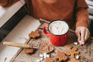 Children drink cocoa with marshmallows and christmas gingerbread man on a wooden background. Christmas sweets with cocoa and marshmallows for children. Winter vacation at home photo