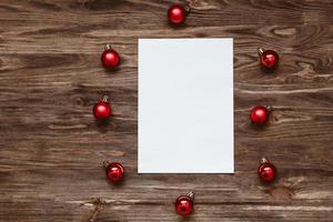 A blank sheet of paper and and red Christmas balls on a wooden background. Top view, flat lay photo