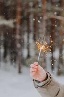 mano sostiene una bengala en el fondo de un bosque de invierno, durante una nevada. celebrando el año nuevo. vacaciones de invierno en el norte. clima nevado foto