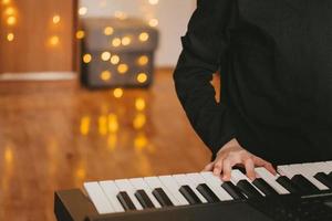 a child's hand plays the digital piano, against the background of a Christmas garland. The child plays the synthesizer. Child's musical hobby. The creative process at home. photo