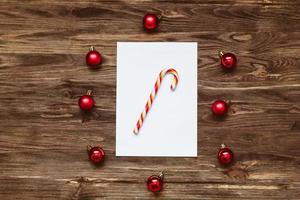 piruleta rayada en una hoja de papel en blanco y bolas de navidad rojas sobre un fondo de madera. vista superior, endecha plana foto