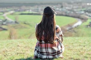 a girl sits with her back on a hill, enjoys a beautiful view photo