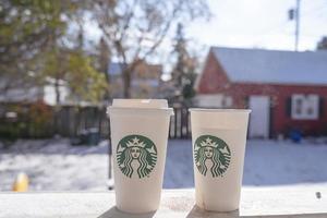 Marinette,WI,USA - Nov14, 2019- Cups of Starbucks Hot Coffee put on white snow in winter garden, fresh and hot beverage take away concept.Starbucks Cafe Coffee Shop. photo