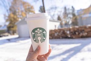 Marinette,WI,USA - Nov14, 2019- Cups of Starbucks Hot Coffee put on white snow in winter garden, fresh and hot beverage take away concept.Starbucks Cafe Coffee Shop. photo