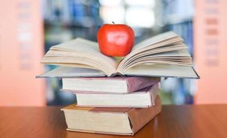 una manzana en los libros sobre la mesa con una estantería en el fondo de las estanterías de la biblioteca - concepto de aprendizaje educativo pila de libros abiertos foto