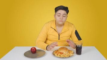 niño obeso eligiendo entre hamburguesa y manzana. elección de alimentos saludables. video