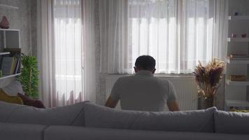 el hombre solo en casa camina hacia la ventana. el solitario se aburre en casa y va a mirar por la ventana. video