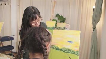 une enseignante asiatique enseigne et démontre à une petite étudiante sur une peinture acrylique couleur sur toile dans une salle de classe d'art, apprenant de manière créative avec compétence à l'école primaire. video