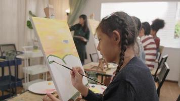 une petite fille se concentre sur la peinture acrylique couleur sur toile avec des enfants multiraciaux dans une classe d'art, l'apprentissage créatif avec des talents et des compétences dans l'enseignement en studio de l'école primaire.