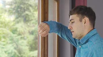 hombre pensativo y aburrido mirando por la ventana. el hombre que apoya la cabeza contra la ventana mira tristemente por la ventana. video