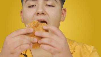 Salute problema, obesità. arancia sfondo. obeso ragazzo mangia Hamburger. lui è avendo divertimento e lui è Grasso. arancia sfondo. video