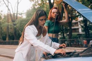 dos mujeres con auto roto en la carretera. capucha abierta foto