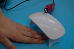 The process of making a beautiful manicure on the hands on the fingers with the help of a special machine and a lamp for drying the varnish in the nail beauty salon on a blue background photo