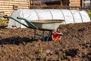carro para transportar carga e invernadero para pepinos en el jardín en primavera, herramienta para jardinería y agricultura doméstica foto