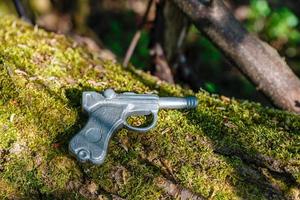 pistola de juguete, pistola de juguete hecha de plomo yace sobre un viejo árbol con musgo. foto
