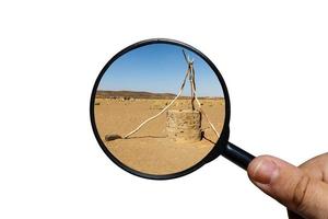 pozo de agua en el desierto del sahara, vista a través de una lupa sobre un fondo blanco, lupa en la mano. foto