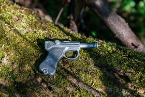 pistola de juguete hecha de plomo yace en un viejo árbol con musgo foto