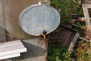 Country washbasin in the garden. An iron tank with a tap hangs on the wall photo