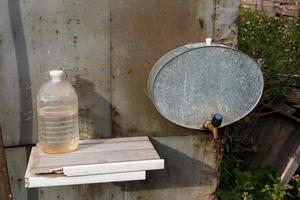 lavabo en el jardín y una botella de agua. lavabo de campo. un tanque de hierro con un grifo cuelga de la pared. foto