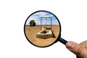 water well in the Sahara desert, view through a magnifying glass on a white background, magnifying glass in hand photo