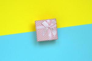 Small pink gift box lie on texture background of fashion pastel blue and yellow colors paper in minimal concept photo