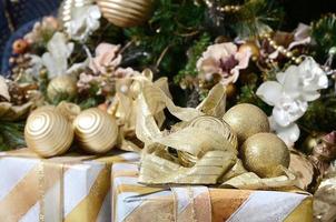 Photo of luxury gift boxes under Christmas tree, New Year home decorations, golden wrapping of Santa presents, festive fir tree decorated with garland, baubles and toys, traditional celebration