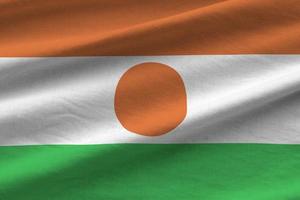 Niger flag with big folds waving close up under the studio light indoors. The official symbols and colors in banner photo