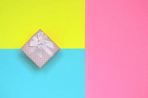 Small pink gift box lie on texture background of fashion pastel blue, yellow and pink colors paper in minimal concept photo