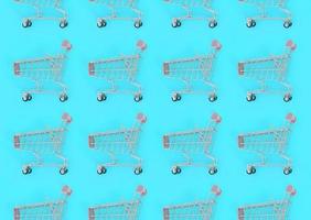 Shopping addiction, shopping lover or shopaholic concept. Many small empty shopping carts perform a pattern on a pastel colored paper background. Flat lay composition, top view photo